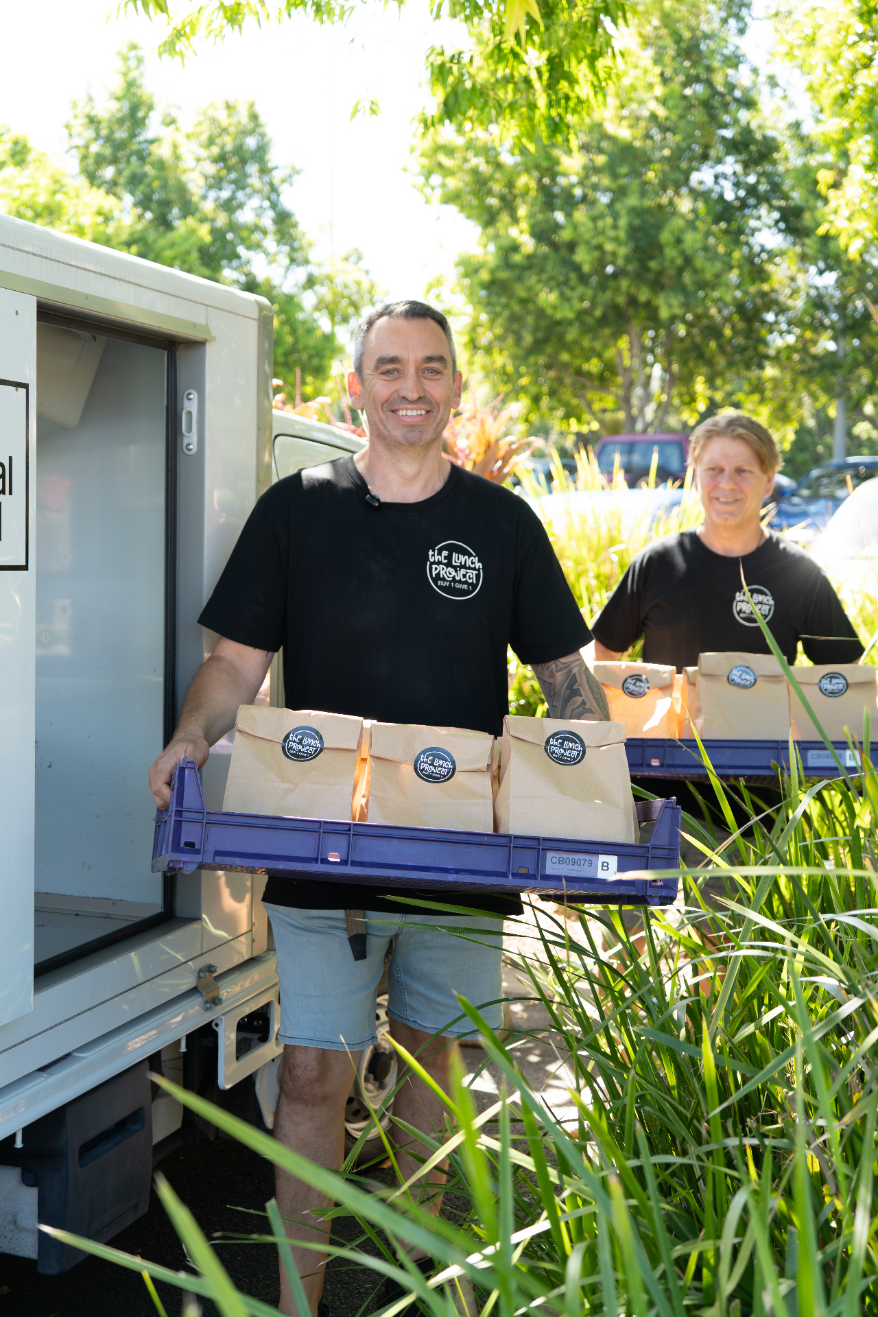 Two Lunch Project volunteers unloading crates of fresh lunches from the delivery van